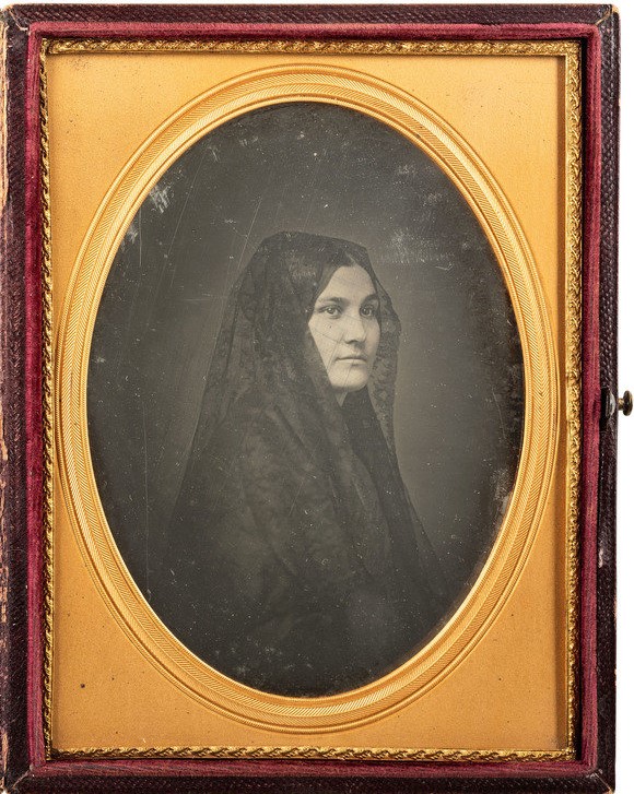 Bust portrait of a young woman, about age 30, in semi-profile, wearing a dark lace mantilla over her head and shoulders